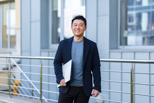 portrait handsome Asian man a university college teacher, businessman, scientist or educator. walks down the city street modern campus with a laptop folder in his hands. goes Outside, outdoor