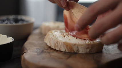 man put prosciutto over cream cheese on slice of ciabatta