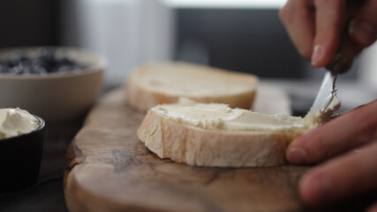 man hand spreading cream cheese on slice of ciabatta