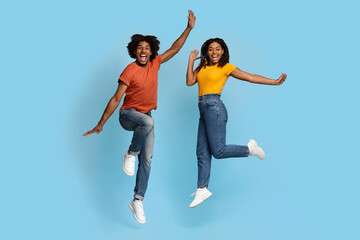 Fototapeta na wymiar Happy african american lovers jumping over blue studio background