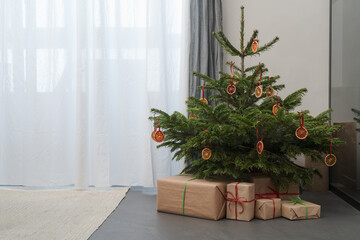 Small christmas tree with gifts in paper wrap near window