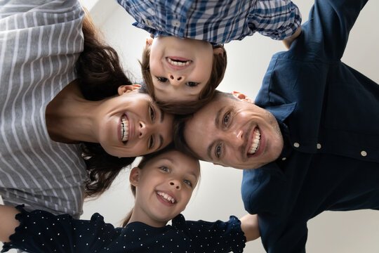 Bottom view faces of happy 35s couple with little adorable son and daughter hugging standing in circle indoors look at camera, having wide toothy smile advertise dental services. Family bond concept