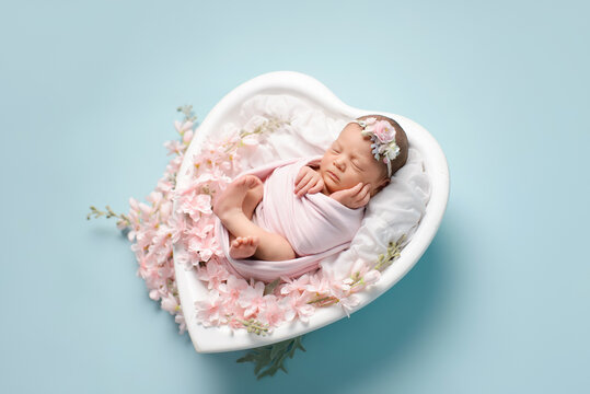 Newborn baby girl sleeping on a crib in the shape of a heart on a blue background. Newborn baby