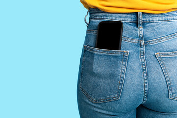 Cropped view of female having cellphone with blank screen in jeans pocket on blue studio background, mockup - obrazy, fototapety, plakaty