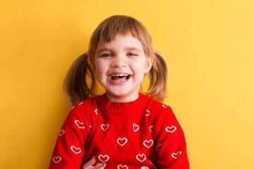 portrait of a laughing child girl in a red sweater on a yellow background. place for text. 

