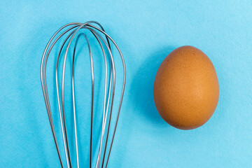 Egg and whisk for whipping on a blue background. Natural products and kitchen equipment.