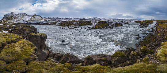 Season changing in southern Highlands of Iceland. Picturesque waterfal Tungnaarfellsfoss panoramic autumn view.  Landmannalaugar mountains under snow cover in far.