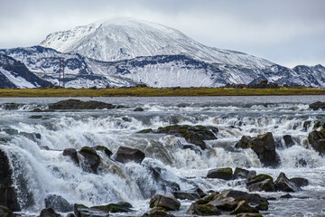 Season changing in southern Highlands of Iceland. Picturesque waterfal Tungnaarfellsfoss panoramic autumn view.  Landmannalaugar mountains under snow cover in far.