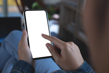 Cell phone mockup image blank white screen. Woman hand holding, using mobile phone during working on laptop computer at home, over shoulder view