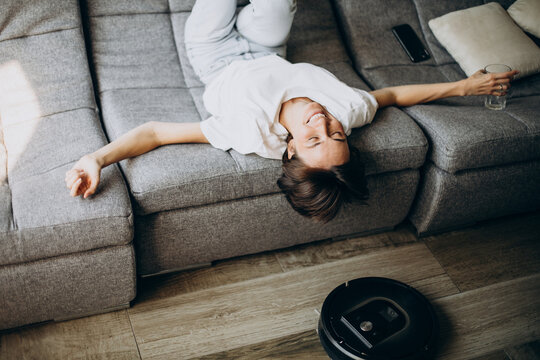 Young woman lying on coach while robot vacuum cleaning floor