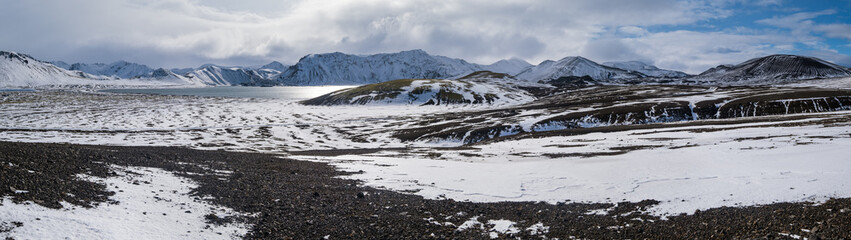 Season changing in southern Highlands of Iceland. Colorful Landmannalaugar mountains under snow cover in autumn. Frostastadavatn lake at the foot of the mountains.