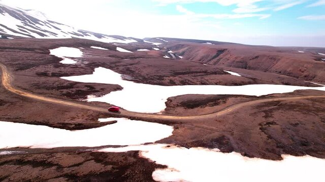 Turning aerial shot in Iceland with vehicles driving in rural snowy mountain landscape. Dirt road, epic landscape. 
