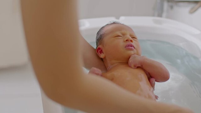 Calm of asian newborn baby bathing in bathtub.mother bathing her son in warm water.adorable newborn infant smile in tub relax and comfortable.Newborn baby care concept