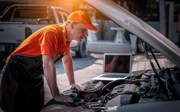 Car mechanic open hood to repair and check car problem system by laptop for maintenance and fixed in garage.