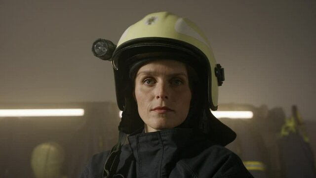 Mid adult female firefighter looking at camera indoors in fire station at night.