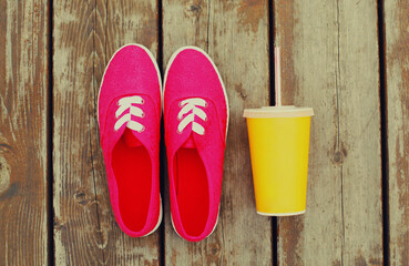 Summer image of pink gumshoes with cup of juice on a wooden table or floor background, top view