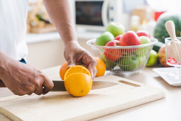 Healthy living and Vegan food. Cooking vegan food. A man is cutting an orange on a wooden cutting board.