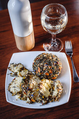 French spicy Boulette d'Avesnes cheese, sprinkled with various herbs, lies on a white plate, closeup. Breen d'Amour. Cheese composition.