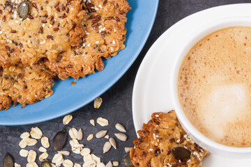 Cup of coffee with milk and fresh baked oatmeal cookies on blue plate. Delicious crunchy dessert