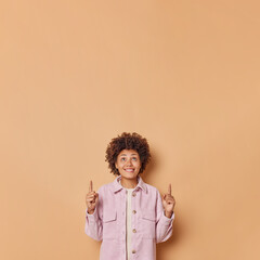 Follow this way. Positive woman in stylish clothes indicates with fore fingers above shows...