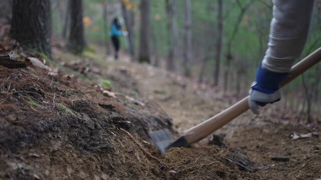 Trail building with metal hoe to make bench cut into hill side, cut roots and clear rocks and dirt for hiking and biking path.