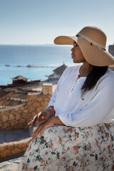 Portrait of beautiful African American model girl in stylish sun hat. Fashion black woman on natural background coast of sea. High quality photo