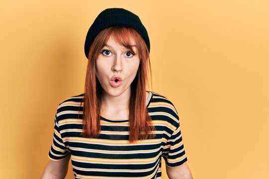 Redhead young woman wearing wool cap scared and amazed with open mouth for surprise, disbelief face