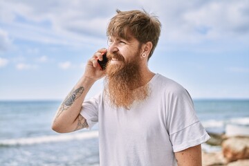 Young redhead man smiling happy talking on the smarphone at the beach.