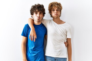 Fototapeta premium Young gay couple standing together over isolated background puffing cheeks with funny face. mouth inflated with air, crazy expression.