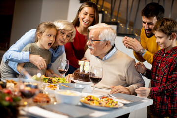 Family celebrating grandfather birthday with cake and candles at home