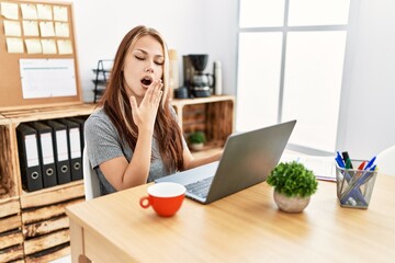 Young brunette woman working at the office with laptop bored yawning tired covering mouth with hand. restless and sleepiness.