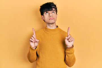 Handsome hipster young man wearing casual yellow sweater pointing up looking sad and upset,...