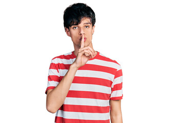 Handsome hipster young man wearing casual striped t shirt asking to be quiet with finger on lips. silence and secret concept.