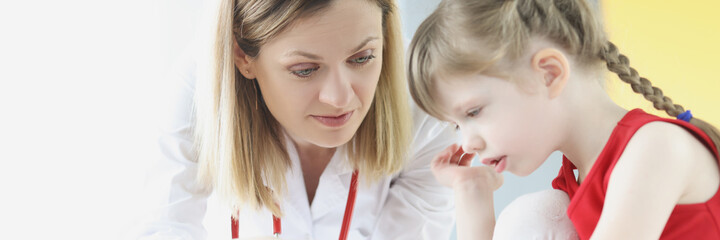Doctor examining skin on hand of little girl using magnifying glass in clinic
