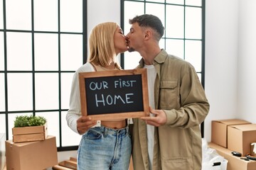 Young caucasian couple kissing and holding blackboard with our first home message at new house