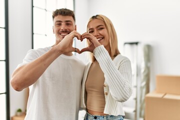 Young caucasian couple smiling happy doing heart symbol with hands at new home.