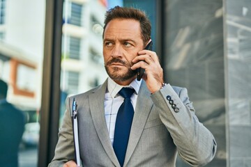 Middle age businessman with serious expression talking on the smartphone at the city.