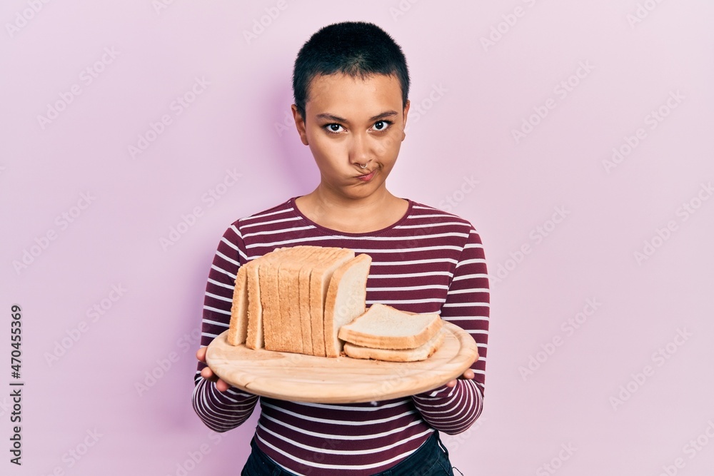 Poster Beautiful hispanic woman with short hair holding sandwich bread skeptic and nervous, frowning upset because of problem. negative person.