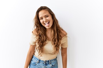 Beautiful hispanic woman standing over isolated while background sticking tongue out happy with funny expression. emotion concept.