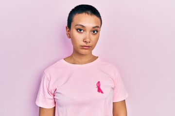 Beautiful hispanic woman with short hair wearing pink cancer ribbon on shirt thinking attitude and sober expression looking self confident