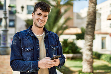 Young hispanic man smiling happy using smartphone at the city