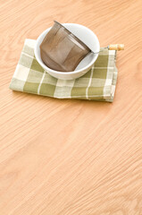 metal tea strainer in a white stoneware bowl on a wooden tabletop background