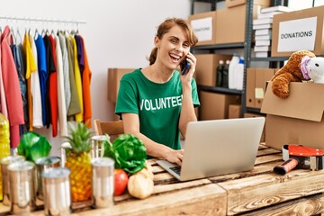 Young caucasian volunteer woman talking on the smartphone using laptop at charity center.