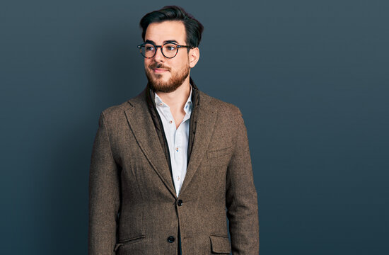 Young hispanic man wearing business jacket and glasses smiling looking to the side and staring away thinking.