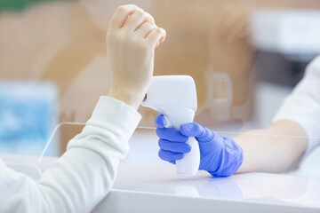 Close up of a female hand being measured body temperature with a contactless thermometer by the employee of the reception desk of a modern hospital. Compliance with measures for the non proliferation