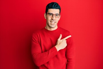 Handsome hispanic man wearing casual clothes and glasses smiling cheerful pointing with hand and finger up to the side