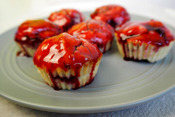 six gluten - free muffins with rice flour cherries and a few cherries and red syrup are on a gray plate . side view. homemade gluten-free cakes