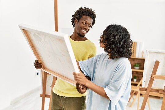 African american artist couple smiling happy holding canvas at art studio.