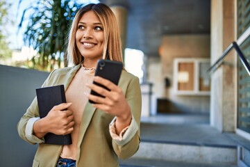 Young latin woman smiling confident using smartphone at street