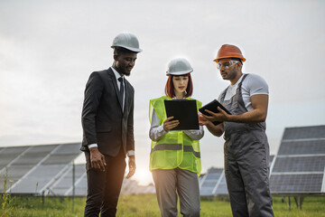 Caucasian woman and african american man doing inspection on solar plant. Indian technician in uniform providing all information about green energy to inspectors.